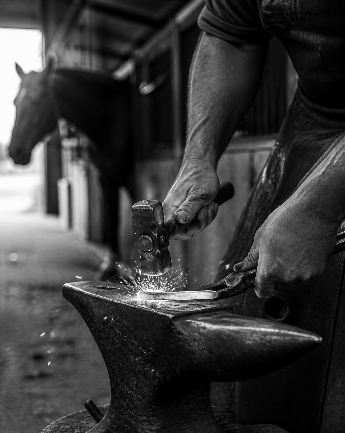 A farrier shaping a shoe in a Kentucky barn aisle